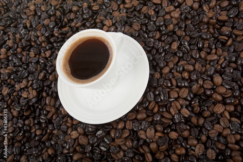 Cup of black coffee on a saucer on roasted coffee beans 