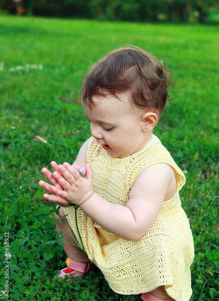 Beautiful baby girl holding flower and looking sitting on green Beautiful baby girl holding flower and looking sitting on green