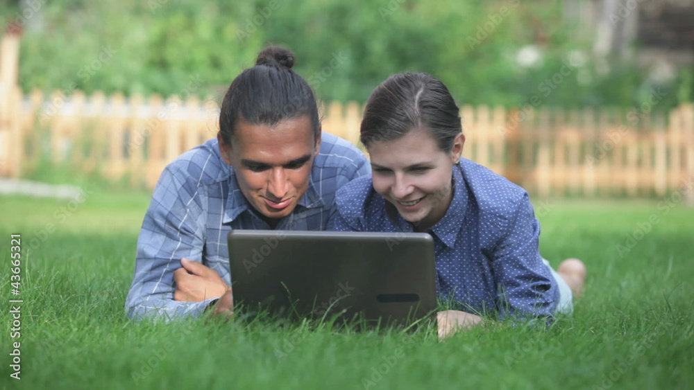 Happy couple lying together and looking at the laptop the meadow Happy couple lying together and looking at the laptop the meadow