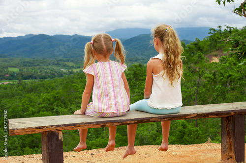 Two girls sit on the bench against the backdrop of the mountains photo