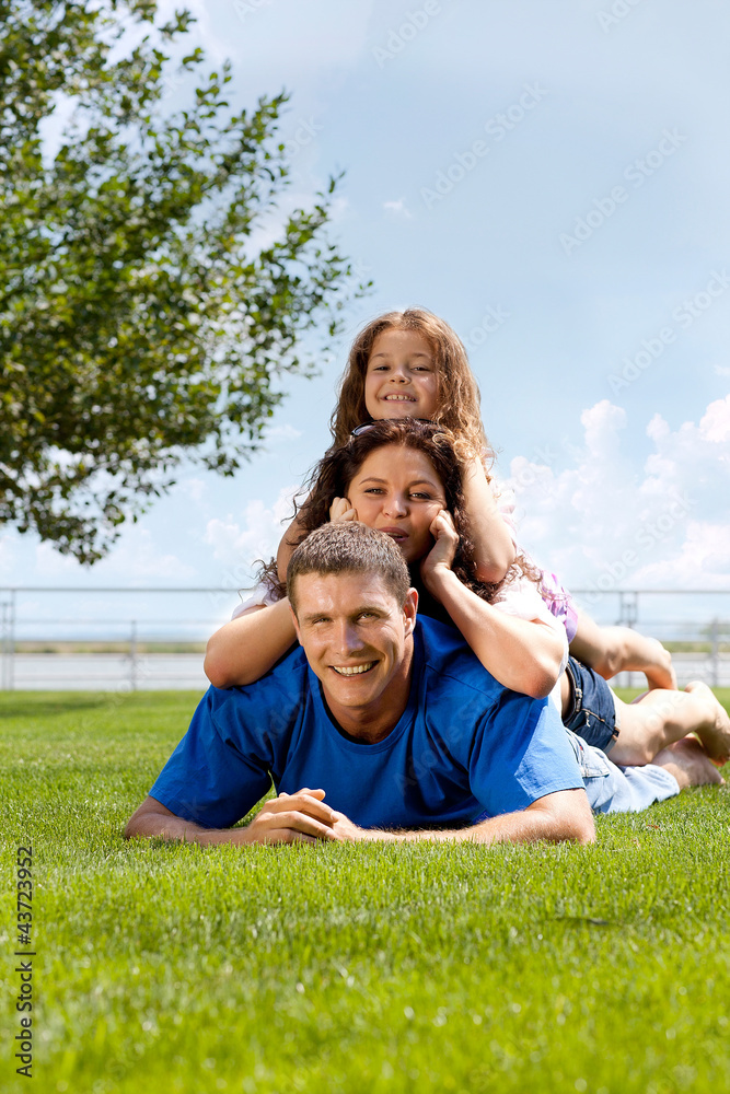 Happy beautiful young family lying on the green grass. Happy beautiful young family lying on the green grass.