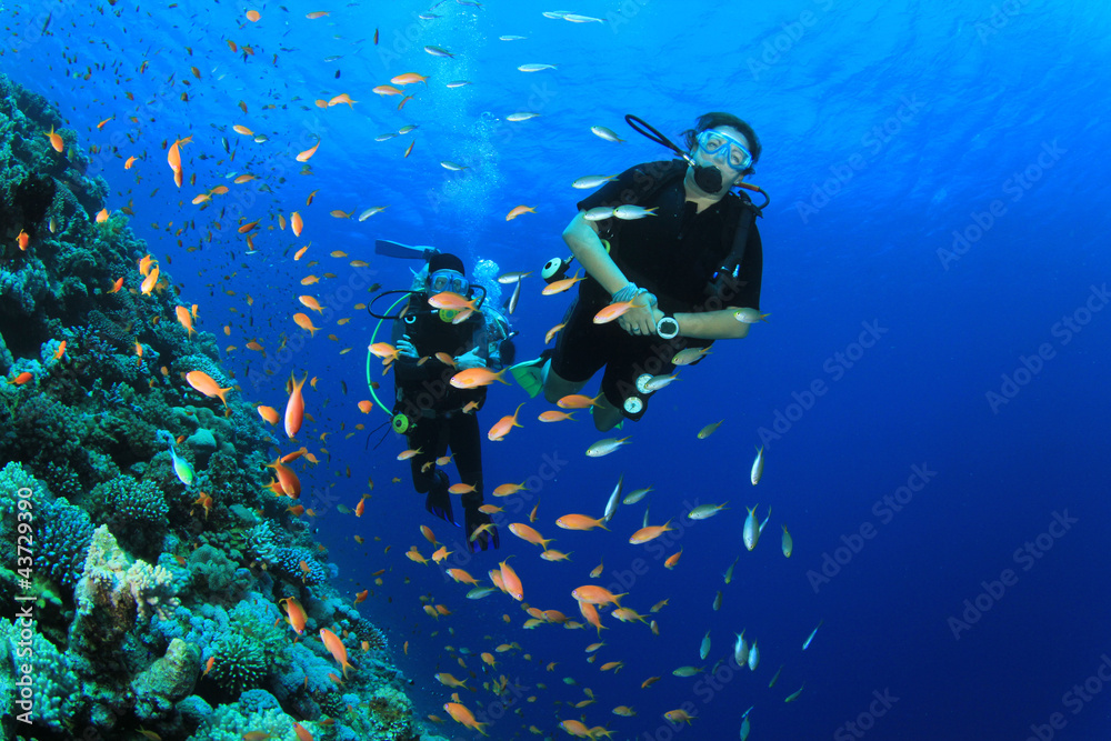 Female Scuba Divers swim through tropical fish on ocean reef Female Scuba Divers swim through tropical fish on ocean reef