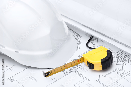 White hard hat and tape measure are on the opened design druft photo