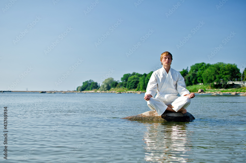 Man in kimono meditating on the rock in the sea