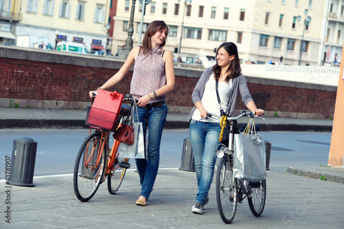 Two Beautiful Women Walking in the City with Bicycles and Bags © Riccardo Piccinini