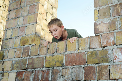 Young boy is looking down over a brick wall, exploring a pit