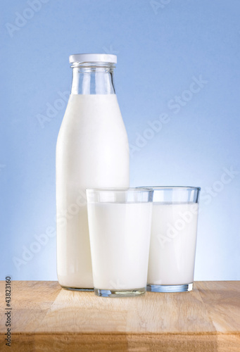 Full Bottle of fresh milk and two glass is wooden table on a blu