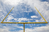 American football goal posts against clouds and blue sky