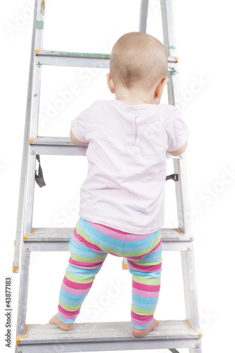 studio shot of a baby girl climbing up a ladder