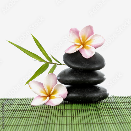 Spa stones and frangipani and a bamboo leaf on green mat