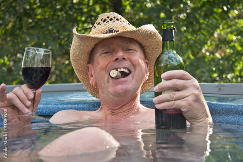 Middle aged man in cowboy hat sitting in hot tub with wine. photo