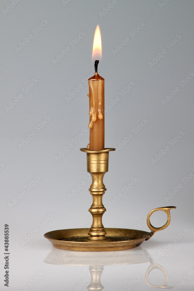 Fototapeta premium Lighted candle in an old brass candlestick, with a gray backgrou