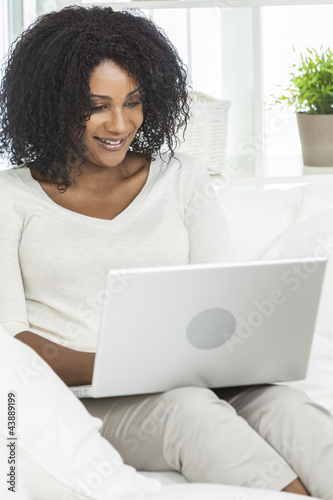 African American Woman Using Laptop Computer At Home on Sofa