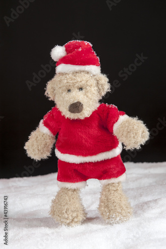 teddy bear in christmas clothes stiandng in the snow