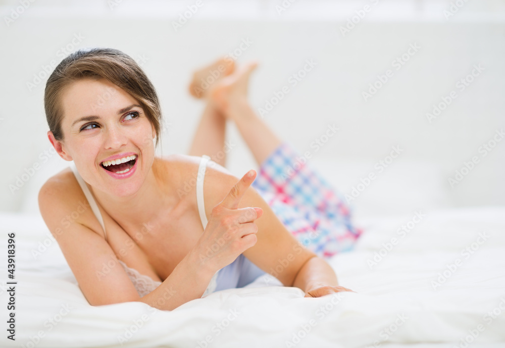 Happy woman laying on bed and pointing on copy space Happy woman laying on bed and pointing on copy space