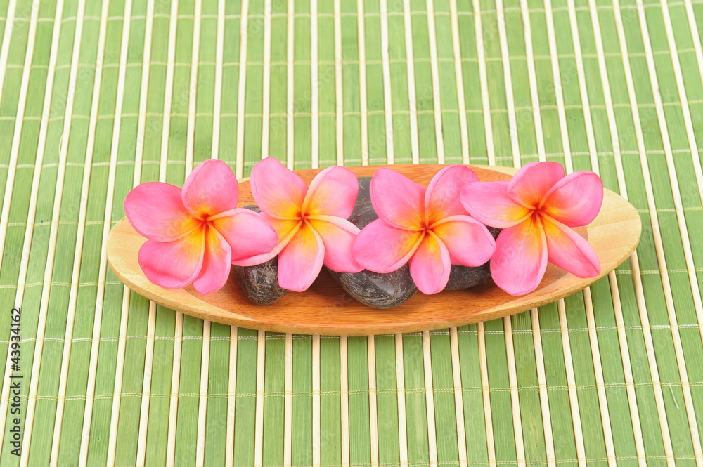 Frangipani and polished stone on bamboo mat Frangipani and polished stone on bamboo mat