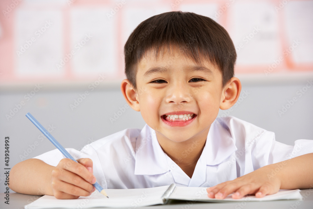 Male Student Working At Desk In Chinese School Classroom Male Student Working At Desk In Chinese School Classroom