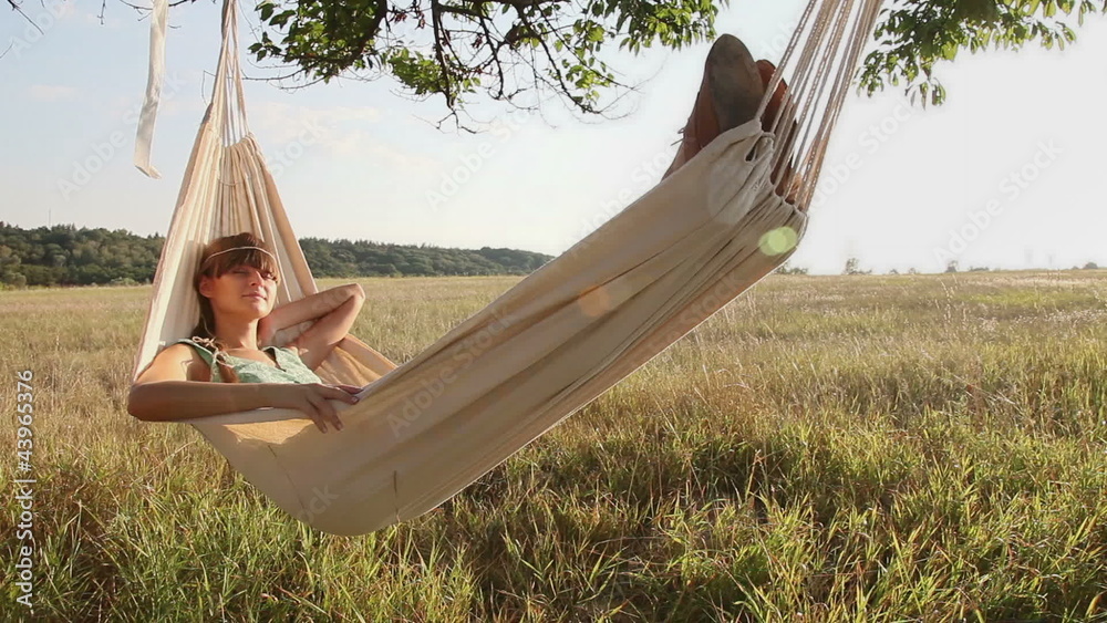 Pretty young girl swinging on hammock at sunset
