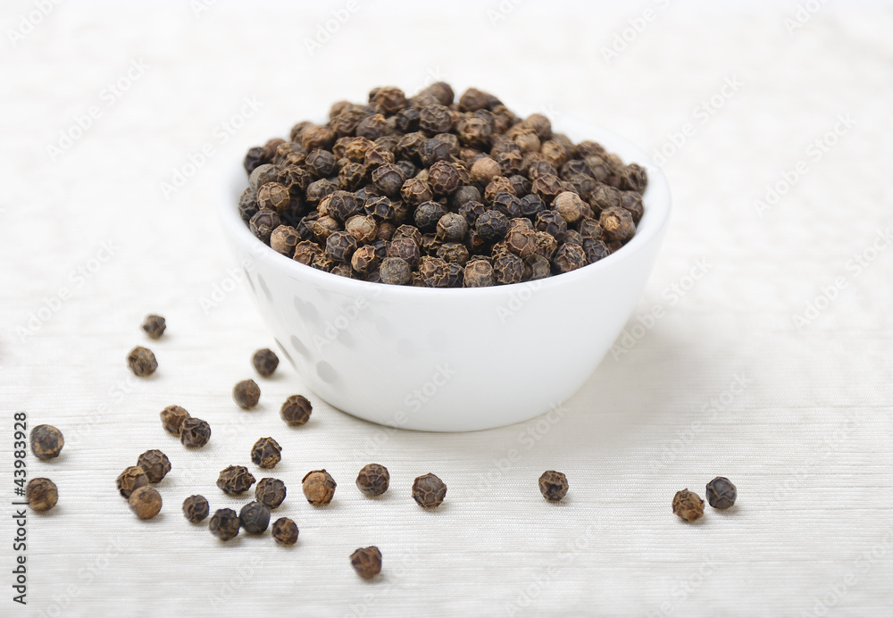 Black pepper. Dried black peppercorns in a white porcelain bowl on white textile made of linen. Macro photo. Black pepper. Dried black peppercorns in a white porcelain bowl on white textile made of linen. Macro photo.