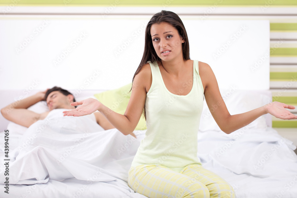 disappointed woman sitting on the bed next to her husband disappointed woman sitting on the bed next to her husband