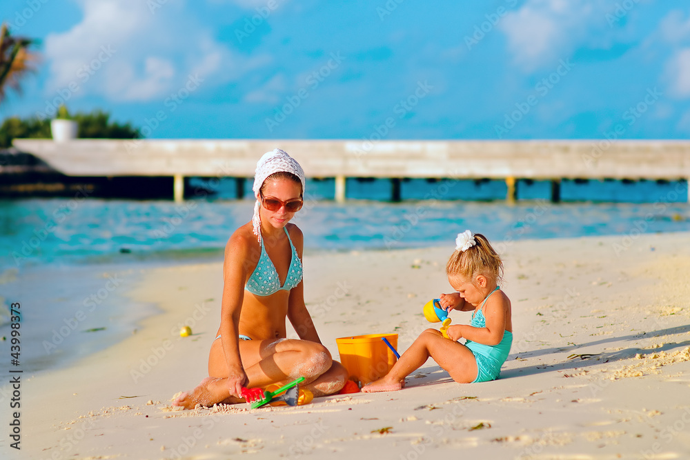 Naklejka premium young beautiful woman and her daughter playing at sandy beach