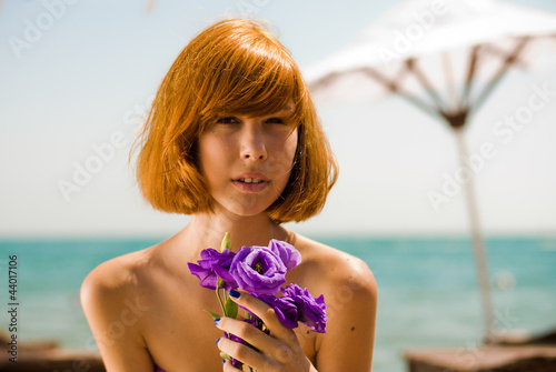Young beautiful woman by blue sea holding purple rose head shot