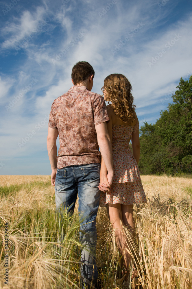 Loving couple holding hands and walking on wheat field