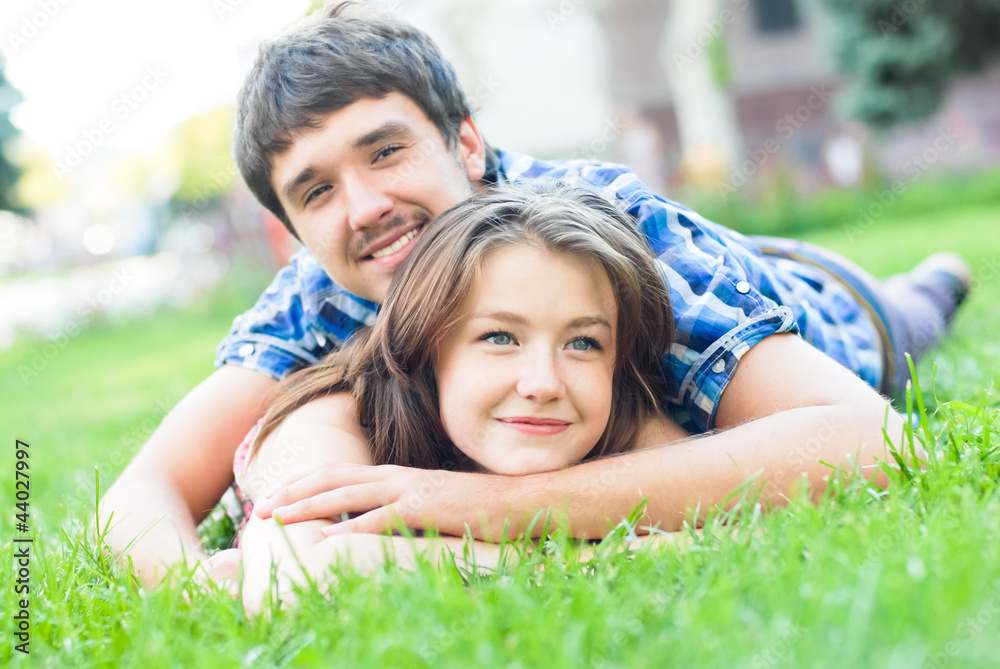 Young happy couple man and woman lying on green lawn and looking Young happy couple man and woman lying on green lawn and looking