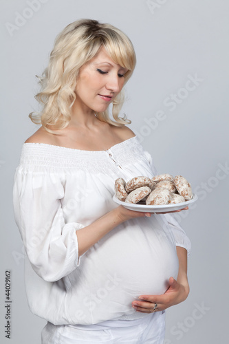 Беременная женщина держит в руках тарелку с пряниками