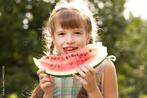 Funny little girl with pigtails eating a watermelon