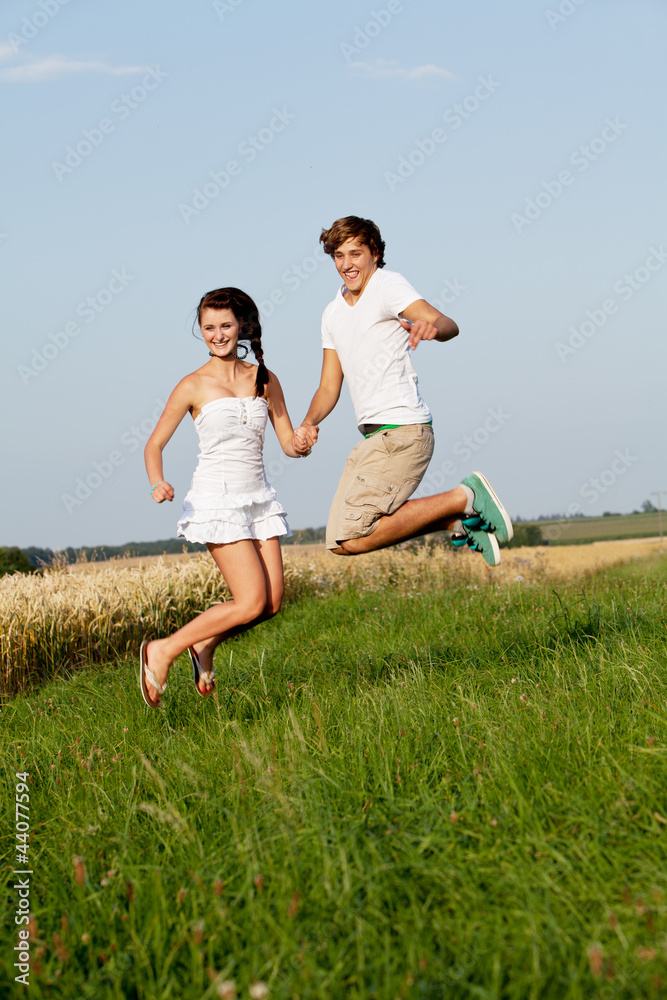 Junges paar springt glücklich in einer Wiese im Sommer Junges paar springt glücklich in einer Wiese im Sommer