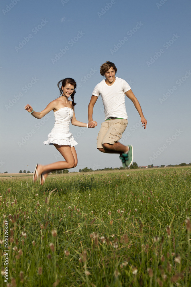 Junges paar springt glücklich in einer Wiese im Sommer Junges paar springt glücklich in einer Wiese im Sommer