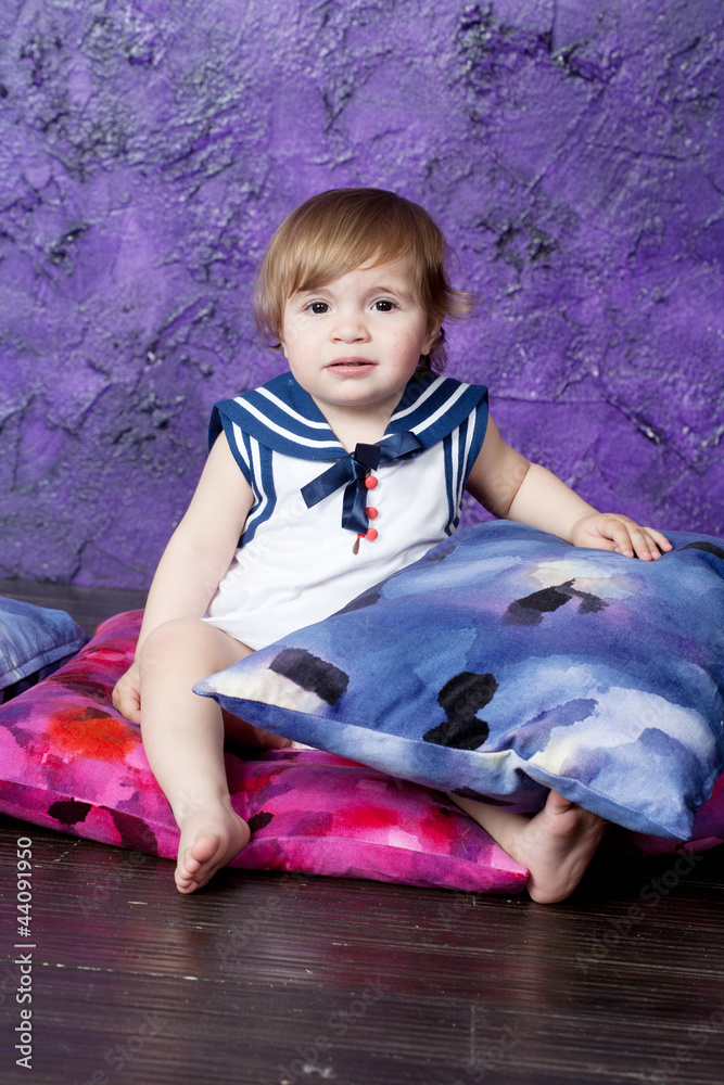 Fototapeta premium little girl in a dress in sea style sits on color pillows