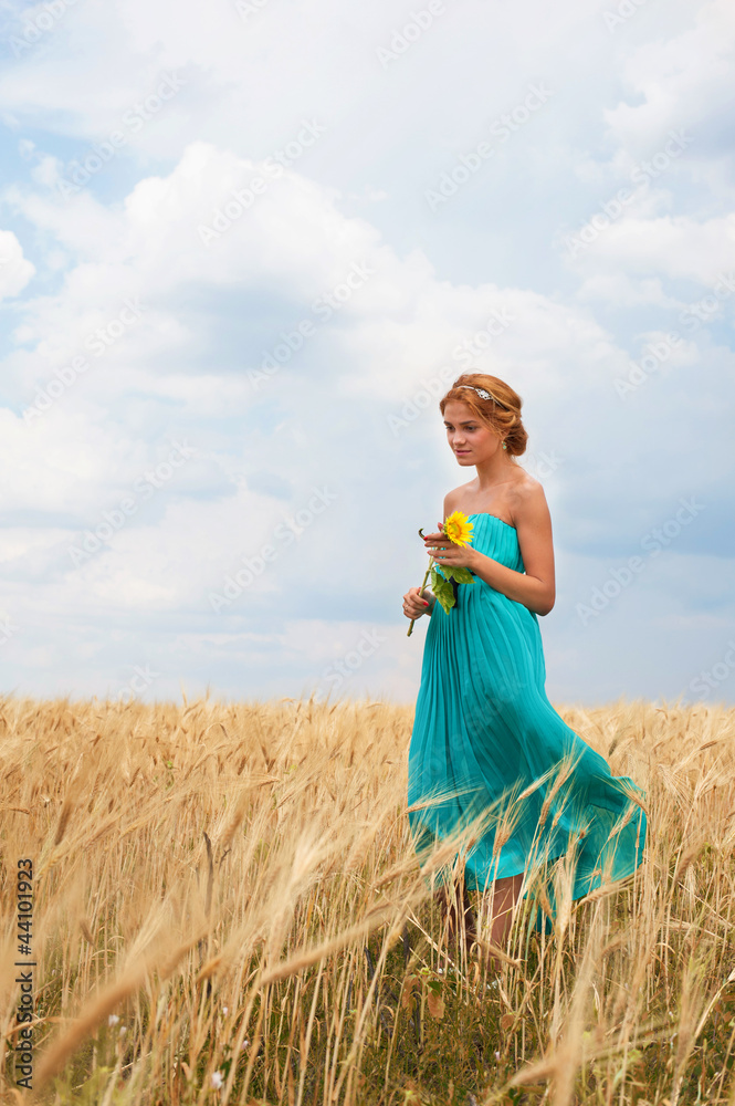 Naklejka premium Pretty girl with sunflower walking through the wheat field