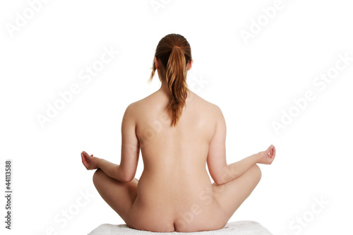 Naked woman is sitting back side in lotos position.