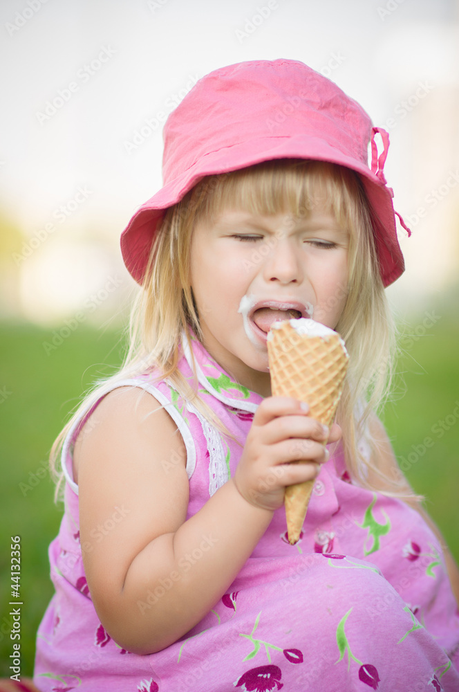Adorable girl in pink hat eat ice cream sitting on grass Adorable girl in pink hat eat ice cream sitting on grass