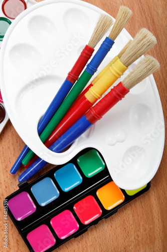 Paint, palette and brushes on a wooden table.