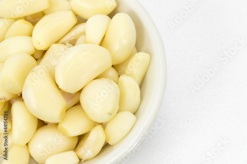 Fresh peeled garlic in a bowl, isolated on white background.