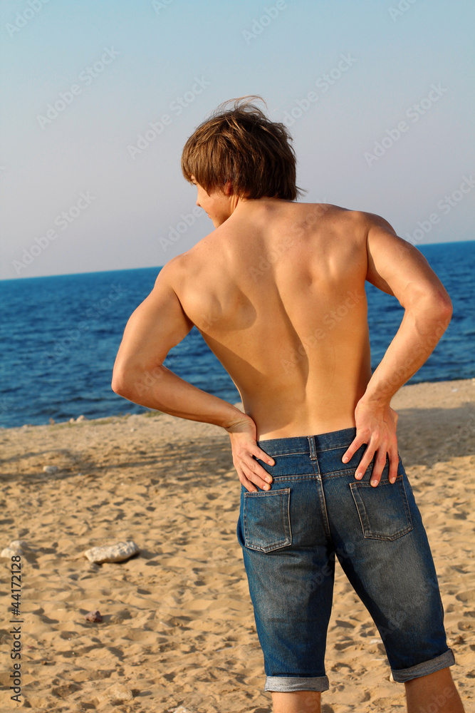 Resting handsome muscular man in jeans on beach
