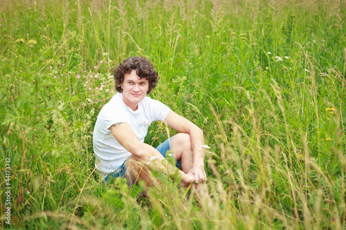 Молодой мужчина сидит на зеленом лугу