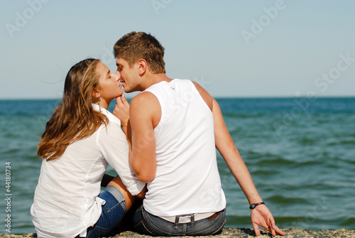 Happy young couple kissing by blue sea over blue sky background