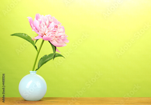 Pink peony in vase on wooden table on green background