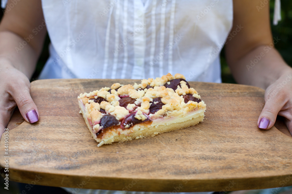 Prune fruit cake on wooden plate with hands