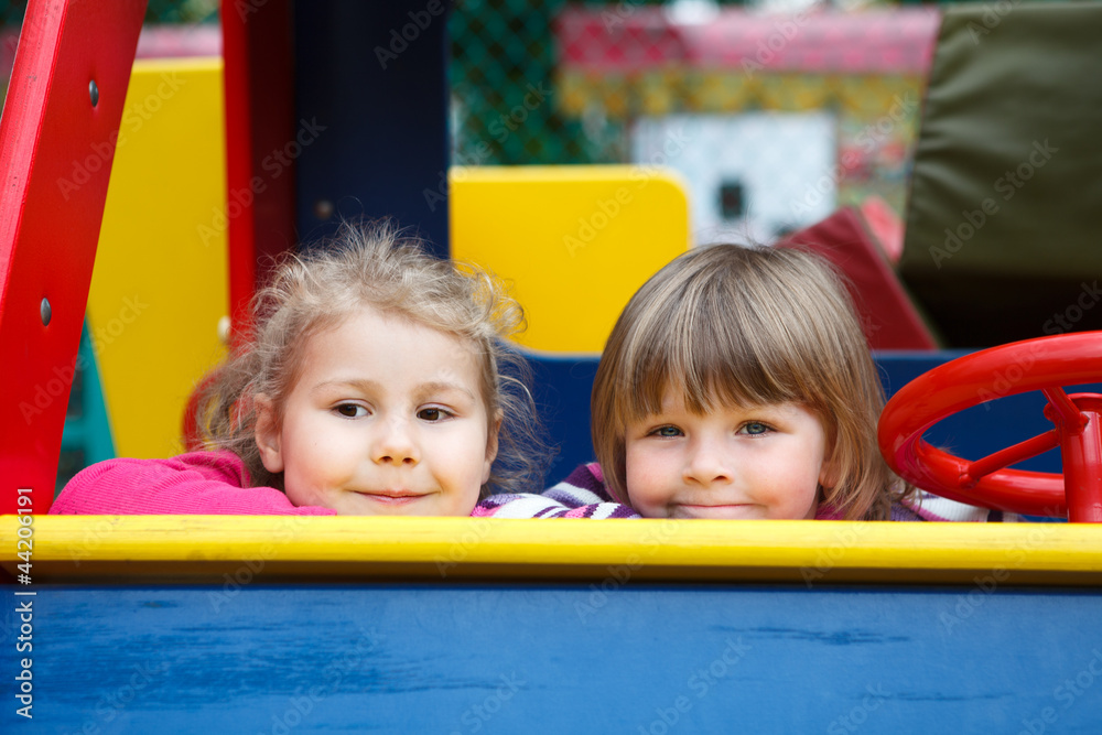 Close up of faces of two happy playful girls sitting in car toy Close up of faces of two happy playful girls sitting in car toy