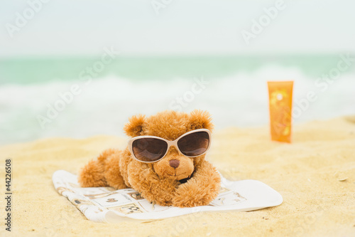 Teddy bear is sunbathing at the beach with sun screen on background