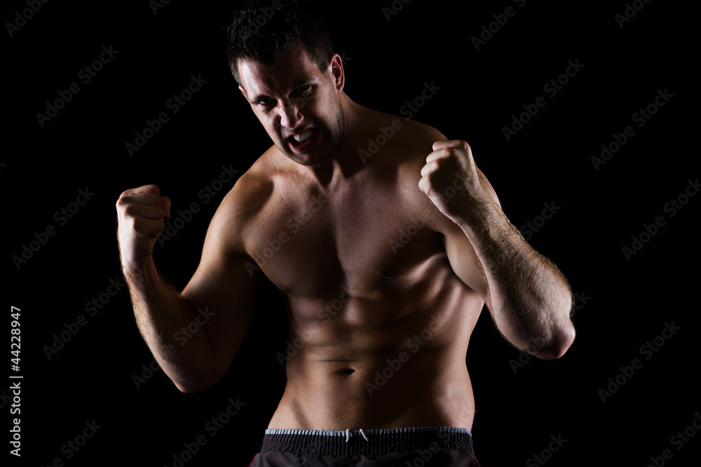 Angry athletic man in attack pose on black
