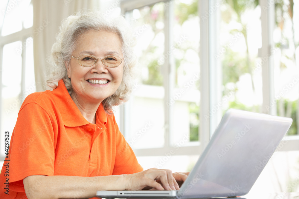 Senior Chinese Woman Sitting At Desk Using Laptop At Home Senior Chinese Woman Sitting At Desk Using Laptop At Home