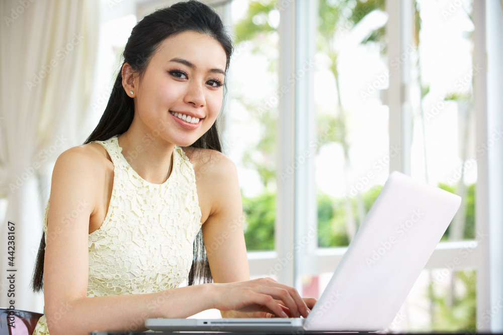 Young Chinese Woman Sitting At Desk Using Laptop At Home Young Chinese Woman Sitting At Desk Using Laptop At Home