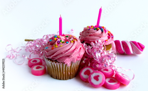 Two pink cupcakes with candy and ribbon on white background