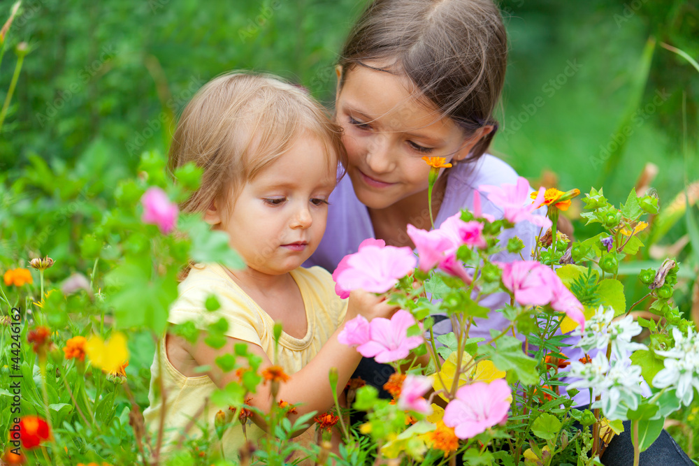 Two adorable sisters among the flowers. Sunny summer day Two adorable sisters among the flowers. Sunny summer day